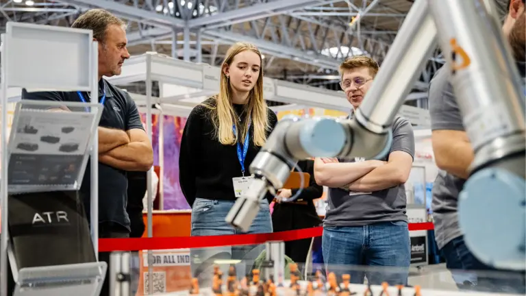 Image of three people in a factory watching a robot create a product