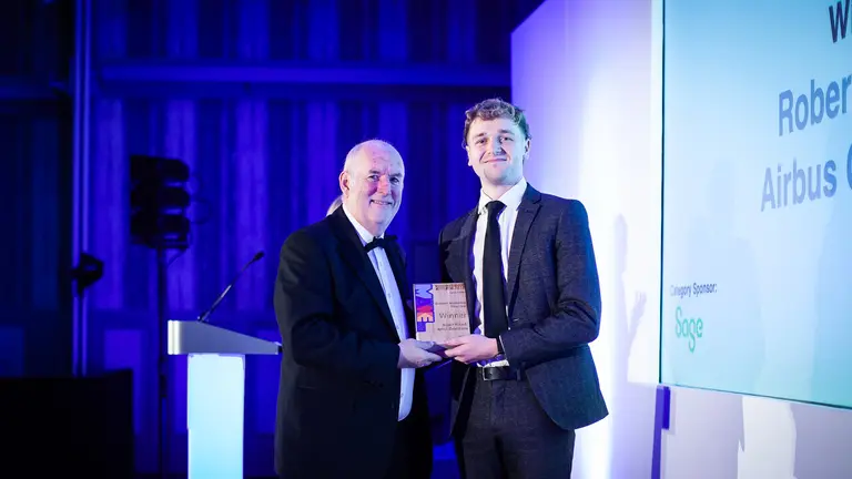 Two men in suits win an award on a stage with blue lighting.