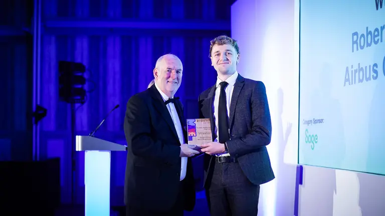 Two men in suits win an award on a stage with blue lighting.