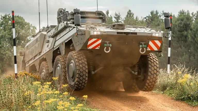 A military vehicle or tank with red and white stripes on the side drives on a dirt path.