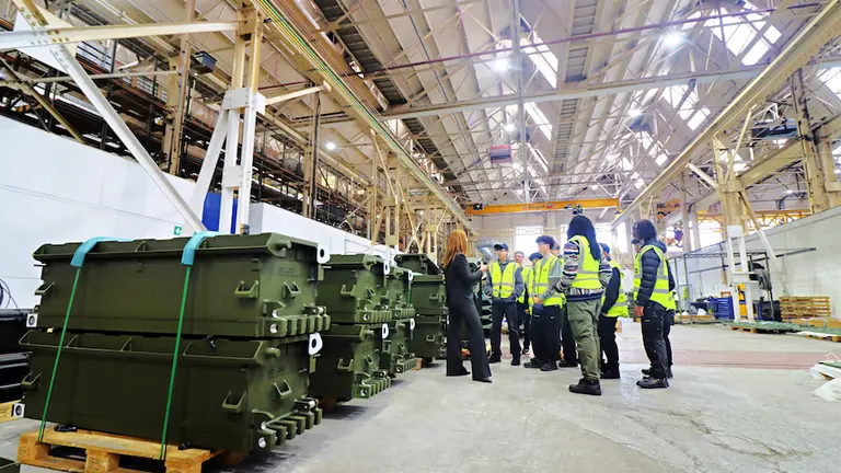 During NMD Several people wearing safety vests view large green military containers in a warehouse.