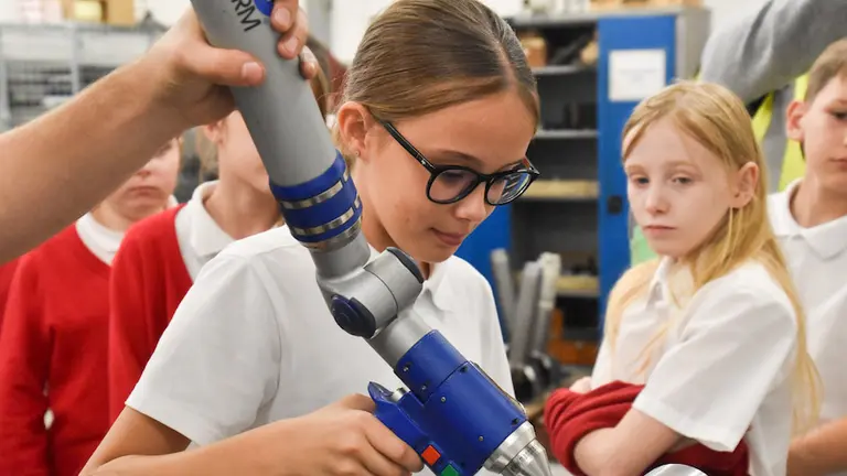 Girl using robotic arm to drill a hole in a metal plate on NMD.