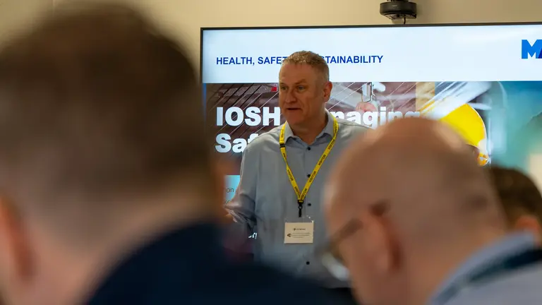 A man wearing a yellow lanyard presents to a group of people at a conference.