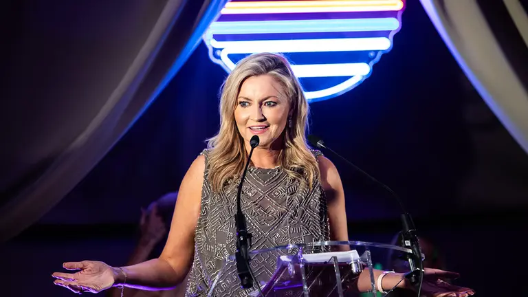 At the Make UK Awards, A woman speaks into a microphone at a podium with her arms outstretched.