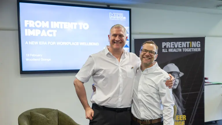 Two men stand next to a poster with the words "From Intent to Impact".