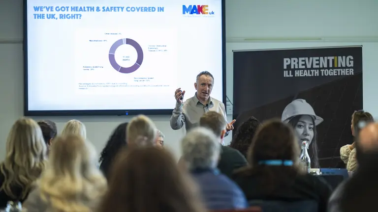 Man in front of a screen speaking to an audience about health and safety.