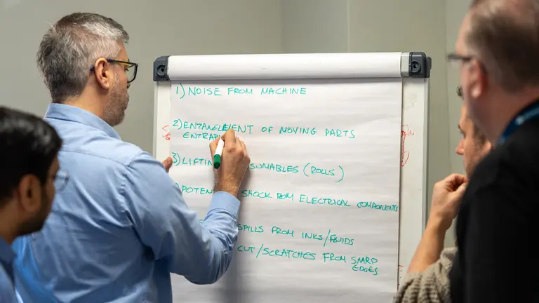 A man writes on a whiteboard with a green marker.