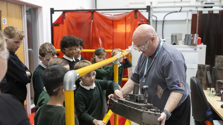 Man with glasses holding an engine part while children look on.