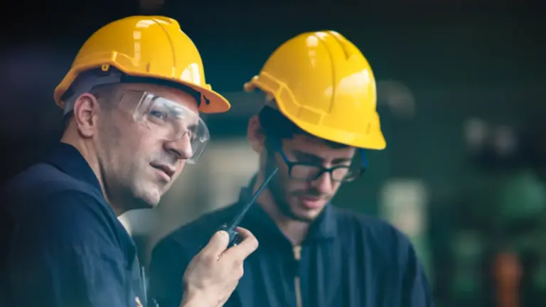 Two men in yellow helmets and blue shirts working in an industrial setting.