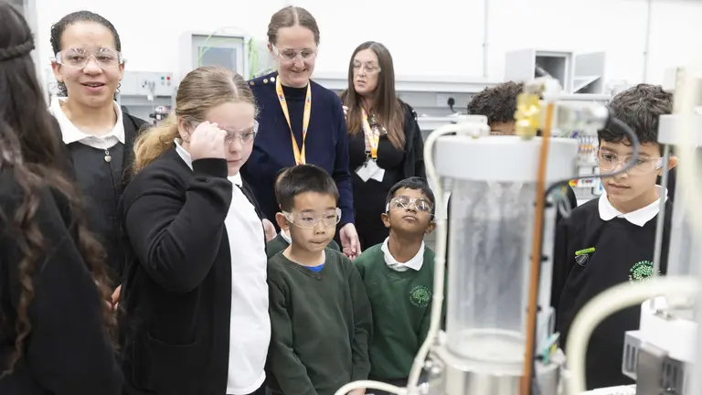 Six primary school children and their teacher look at mechanical device 