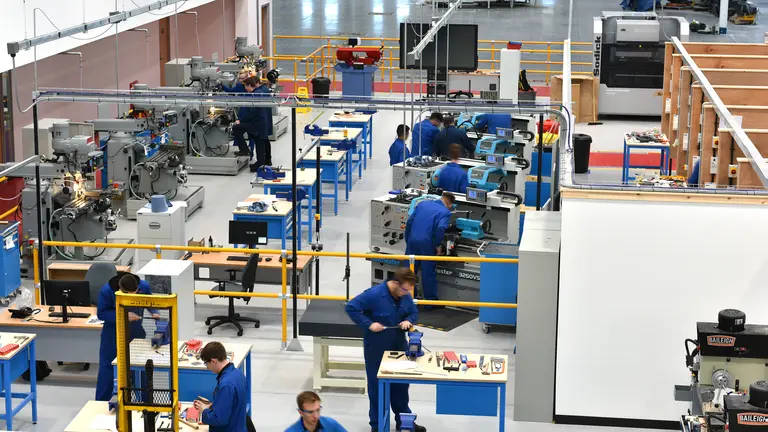 Factory floor with workers in blue uniforms operating various machines.