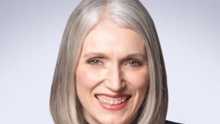 Woman wearing a black turtleneck and gray blazer smiling at the camera.