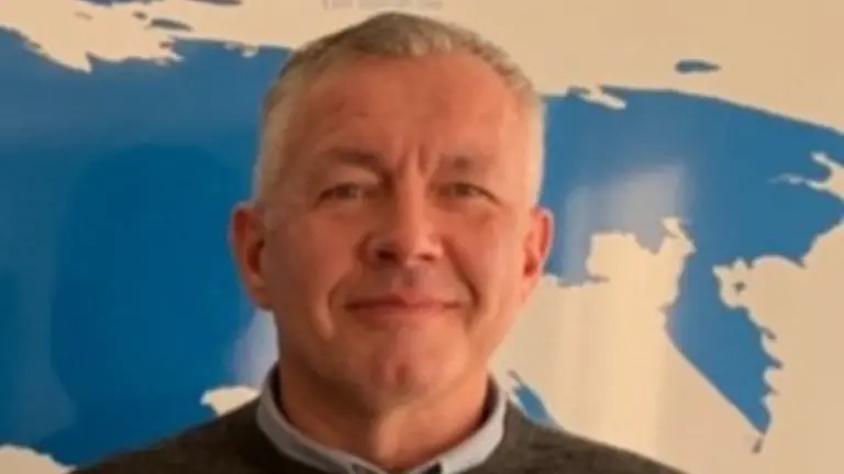 A man in a grey sweater smiling for the camera.