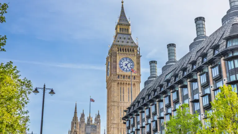 Big Ben clock tower on a sunny day with trees and a building in the background.