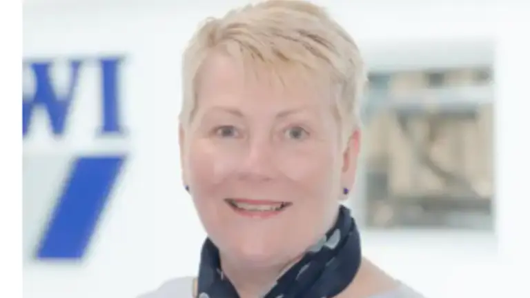 Woman wearing a gray shirt and a scarf smiling at the camera.