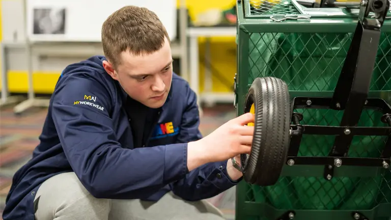 A man in a blue sweatshirt repairs a tire on a green cart.
