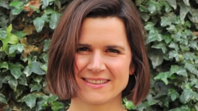 Woman with short brown hair and a checkered top smiling at camera.