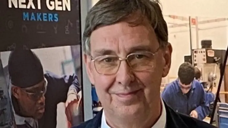 Man in orange tie and glasses smiles in front of a sign.