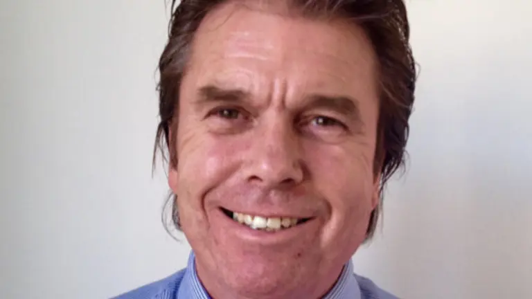 Smiling man with short brown hair in a blue shirt and tie.