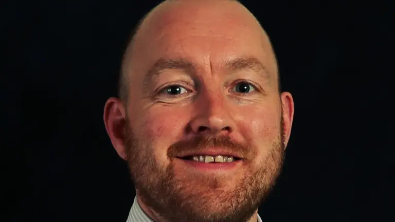 Man in white shirt and blue tie smiling at the camera.