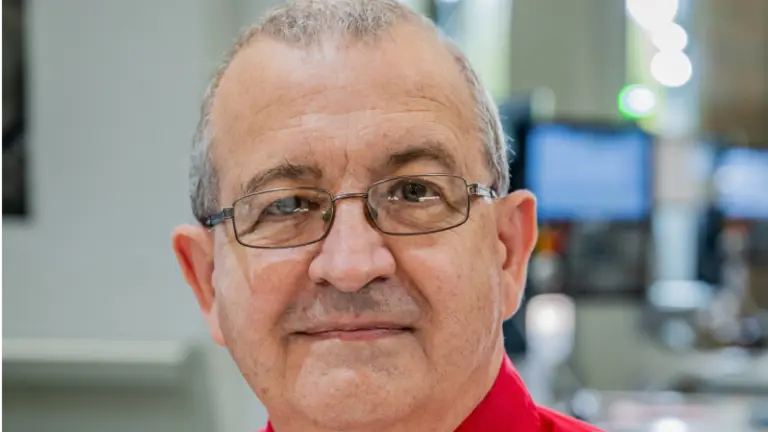 A man wearing glasses and a red shirt smiles for the camera.