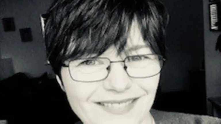 Woman with short hair and glasses smiles at the camera.