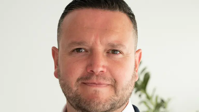 Man in a business suit with plant in the background.