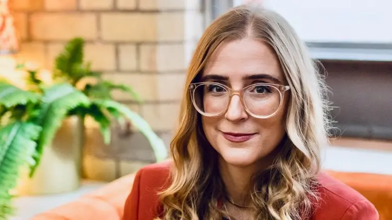 Woman with glasses smiles in a room.