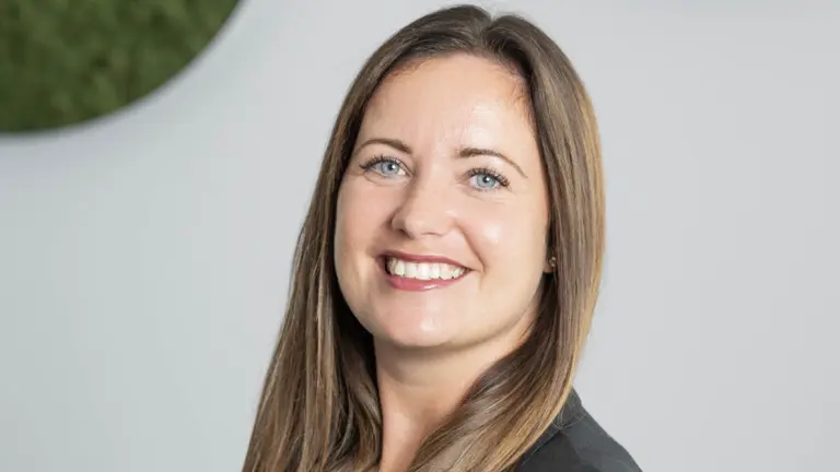 Woman in professional attire smiling at camera with arms crossed.