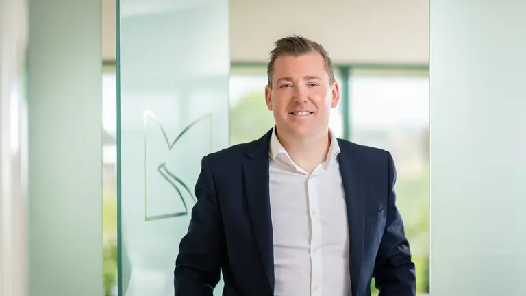 Man in business attire smiling in front of glass wall.