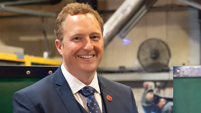 A smiling man in a blue suit and tie stands in a factory.