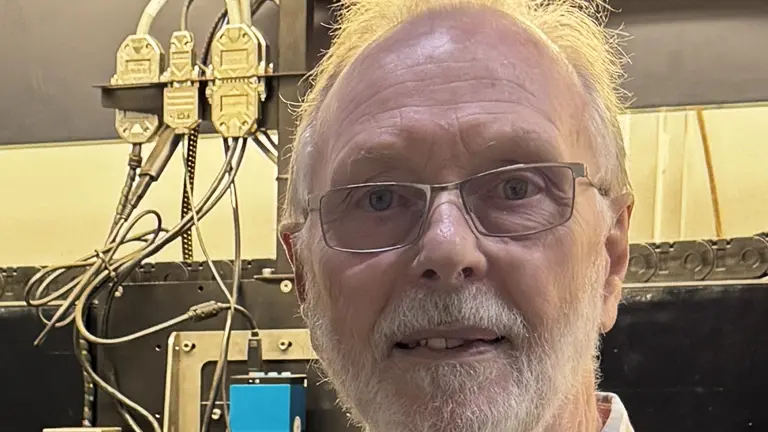 Man with glasses in a workplace, smiling for the camera.
