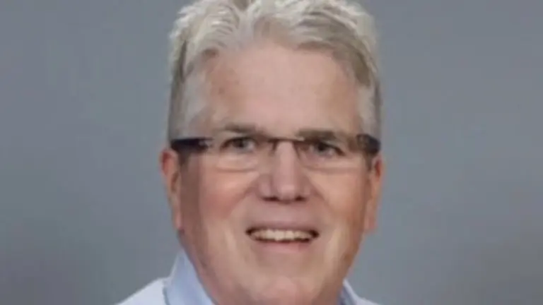 Man in light blue shirt and glasses smiling.