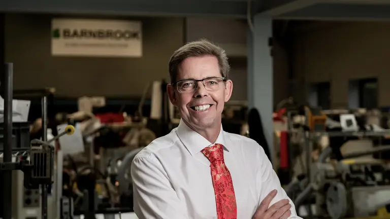 Man in white shirt and red tie standing with arms crossed in a factory.