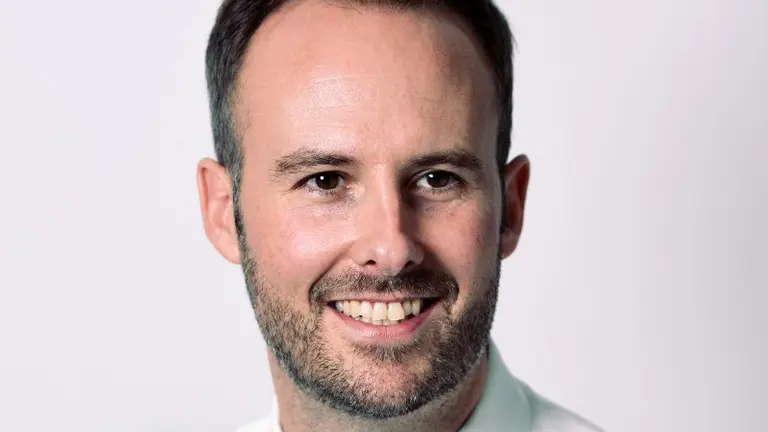 Man in white shirt and blue tie smiling at camera.