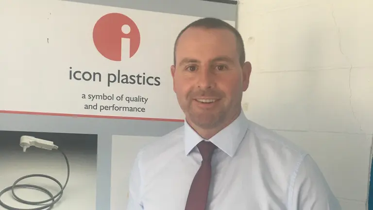 Man in a shirt and tie stands before a sign for Icon Plastics, smiling for the camera..