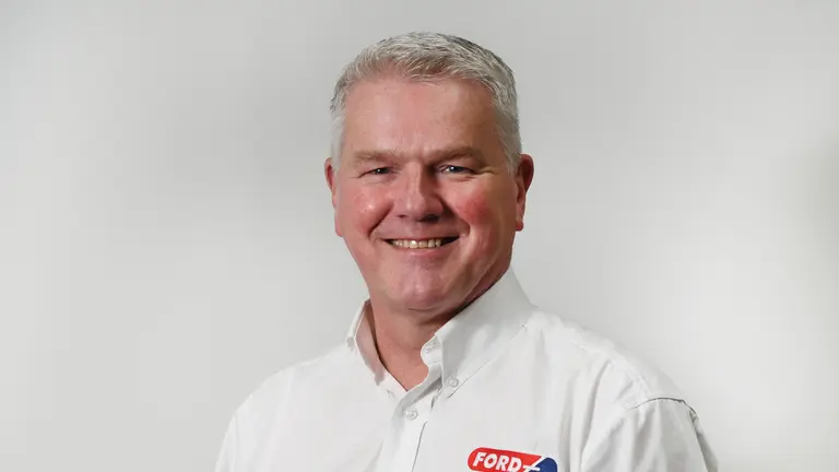 Man in a white shirt with Ford logo, smiling at the camera.