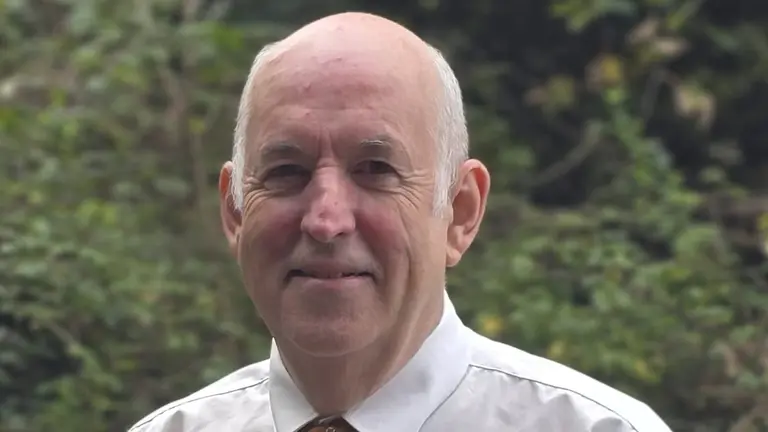 Man with white shirt and orange tie smiling at the camera.