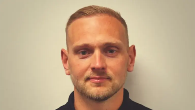 Man with beard and black shirt, smiling at camera.