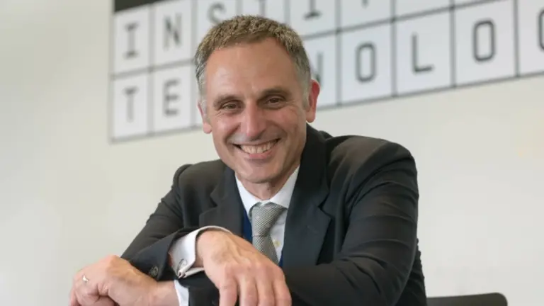 Man in a suit smiling behind a sign that reads "Institute of Technology"