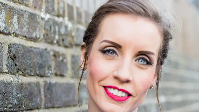 Woman in blue dress with pearl necklace smiles for camera.