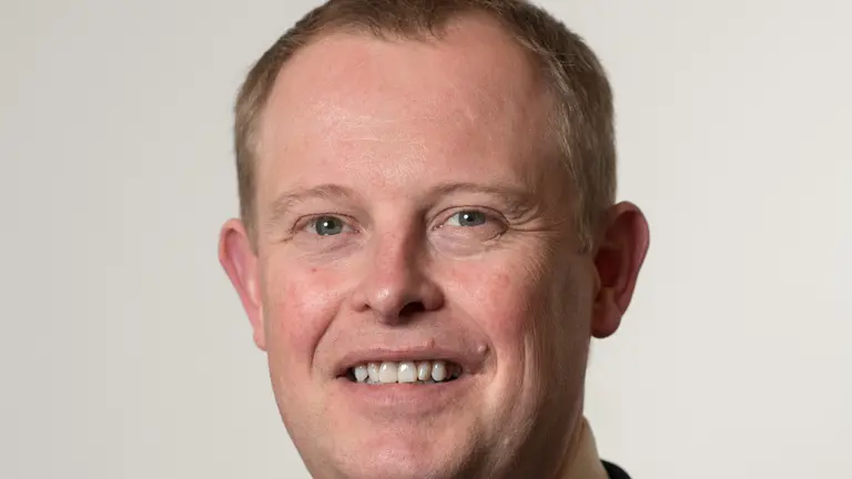A man in a black suit and blue tie smiles for the camera.