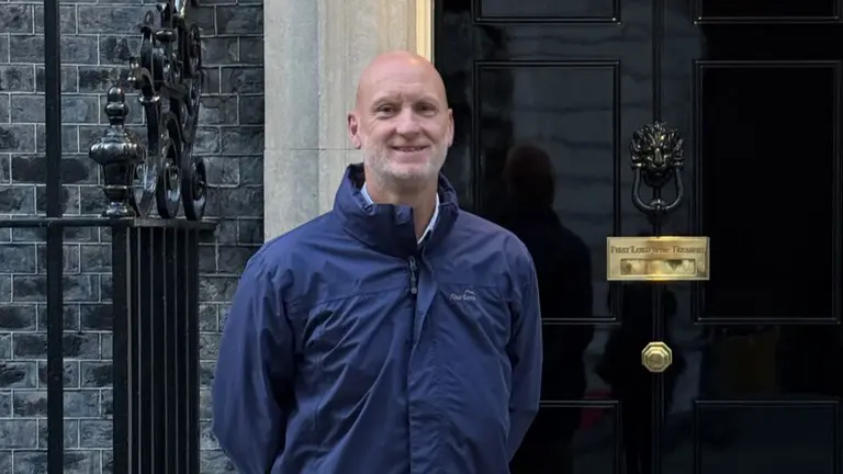 Man in navy blue rain jacket smiling in front of 10 Downing Street