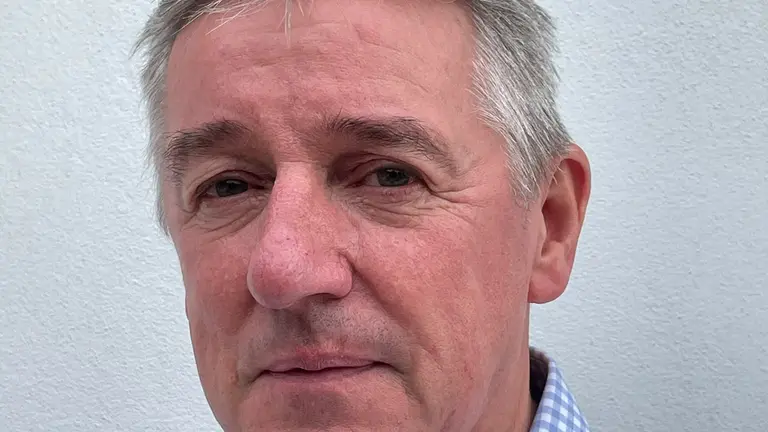 Close up of man in blue checkered shirt looking directly at camera.
