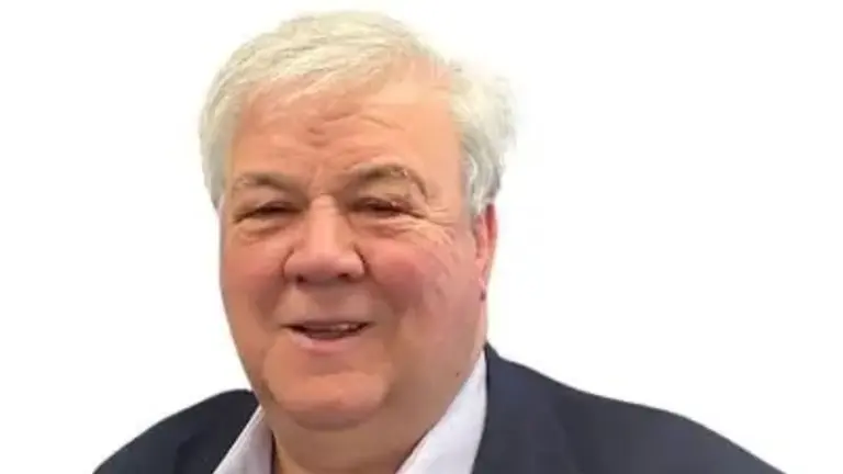 A man wearing a navy blazer and white shirt smiles.