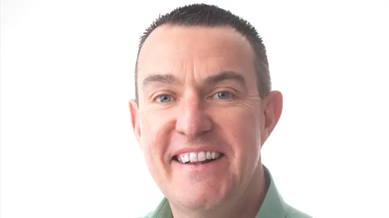 Man in teal shirt smiling with arms folded.