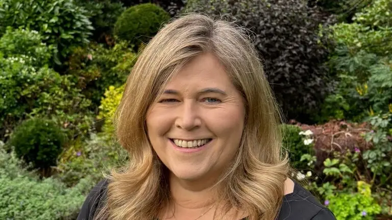 Woman in black shirt smiling in garden.