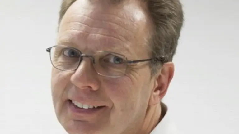 Man in glasses smiling in a white polo shirt.