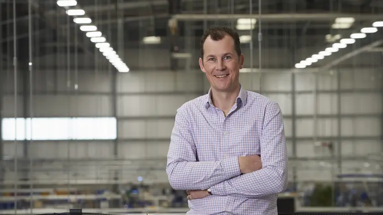 Man smiling with arms crossed in front of a factory.