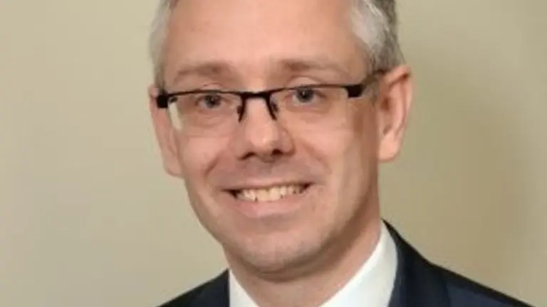 A man in a dark suit and red tie smiles at the camera.